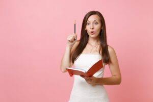 Woman in white holding red book and pen considers marquee wedding plans.