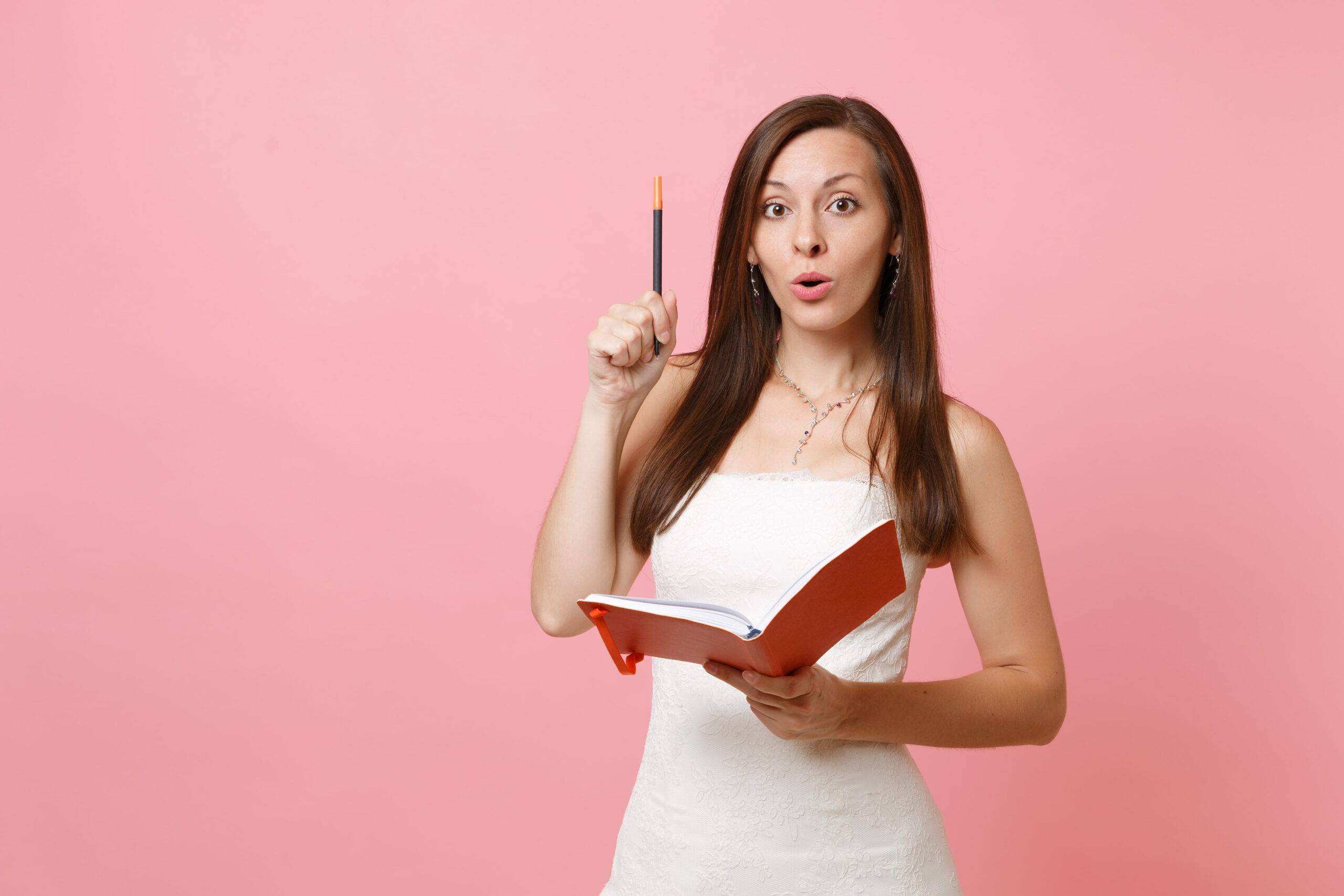 Woman in white holding red book and pen considers marquee wedding plans.