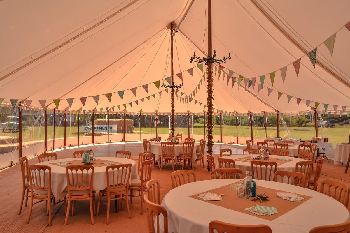 Round tables inside a traditional marquee with bunting, planning a marquee event in the countryside