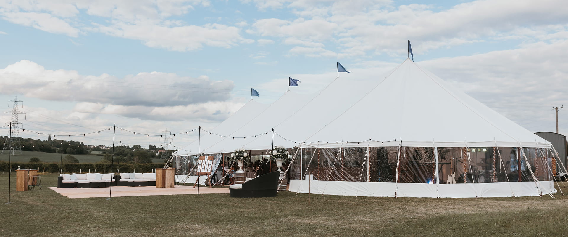 Sailcloth marquee with clear sides and festoon lighting set in the countryside - popular types of marquees for outdoor weddings.