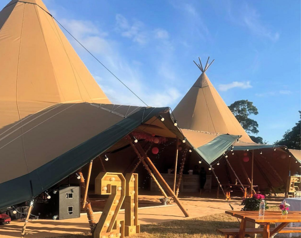 Tipi-style stretch tent with festoon lighting and wooden seating - popular types of marquees for relaxed outdoor events and weddings. 